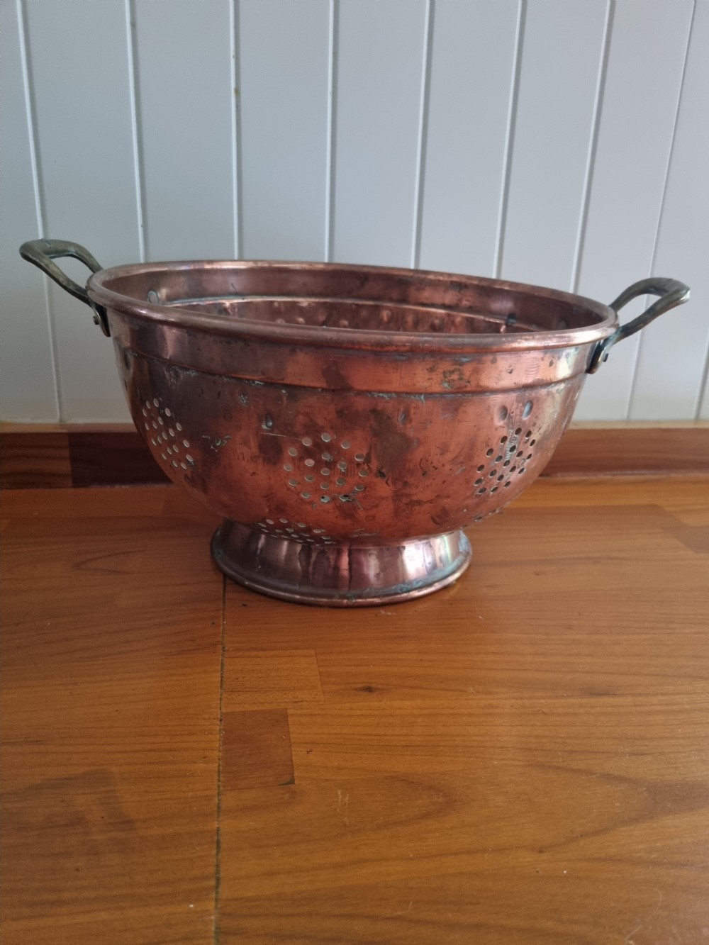 A collection of 19th-century metal kitchenalia featuring a copper colander with brass handles alongside several antique tin graters. View IV