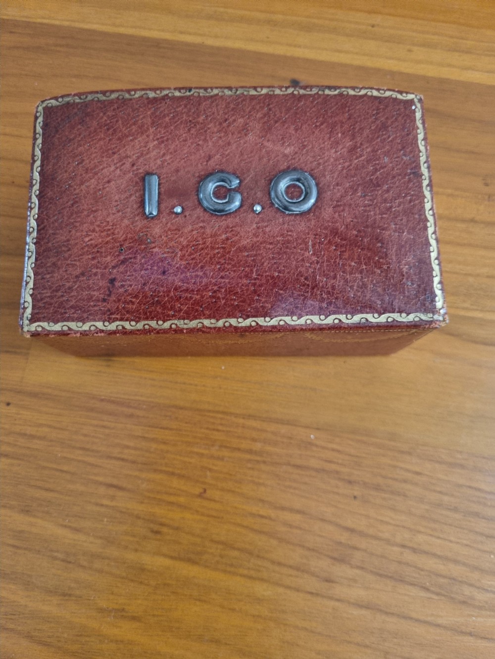 A small rectangular deep red Morocco leather stamp box with gilt festoon decoration and applied metal initials on the lid. View V
