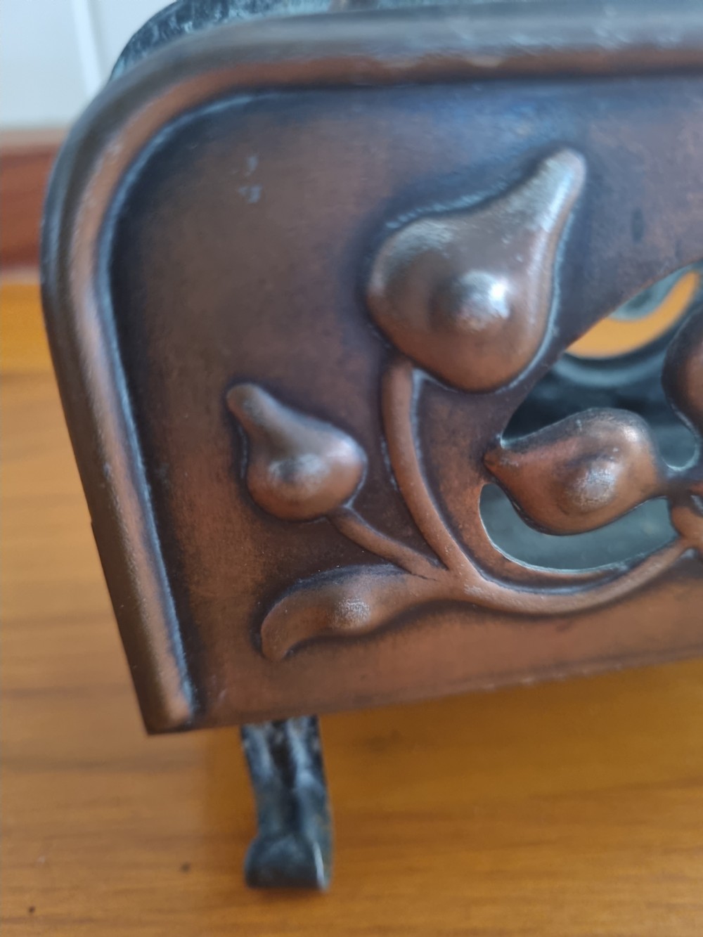 A copper Arts and Crafts letter rack featuring embossed floral motifs, a looped top handle, and four curved legs on a wooden surface. View III