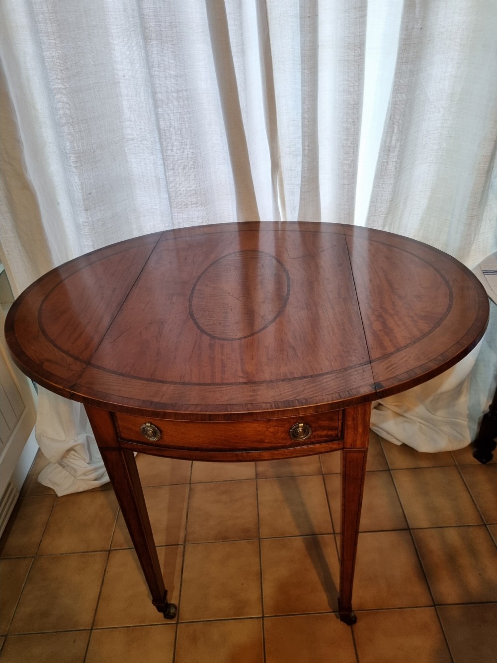 An oval Georgian drop-leaf Pembroke table crafted from inlaid satinwood with a single frieze drawer and square tapered legs on castors. View II