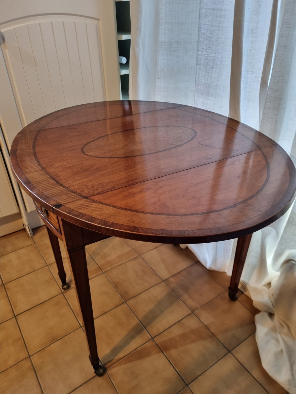 An oval Georgian drop-leaf Pembroke table crafted from inlaid satinwood with a single frieze drawer and square tapered legs on castors. View V