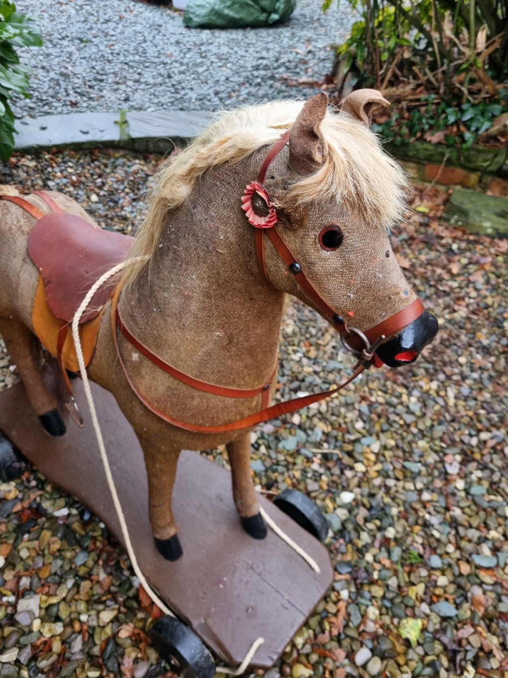 A late 19th-century childs pull-along toy horse with a tan fabric body, blonde mane, leather saddle, and bridle mounted on a brown wooden plinth with four wheels. View III