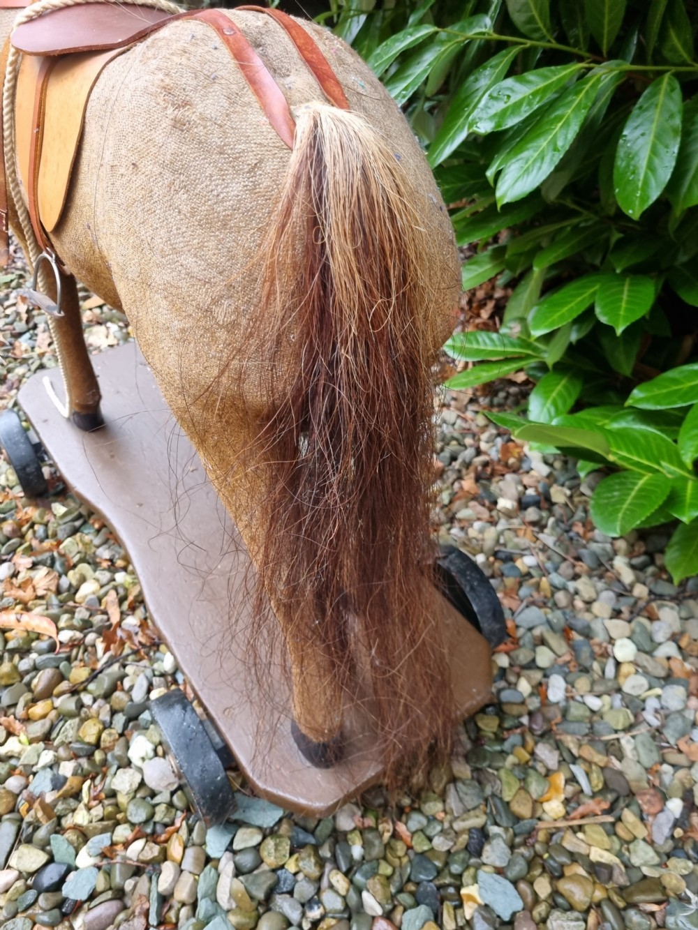A late 19th-century childs pull-along toy horse with a tan fabric body, blonde mane, leather saddle, and bridle mounted on a brown wooden plinth with four wheels. View IV