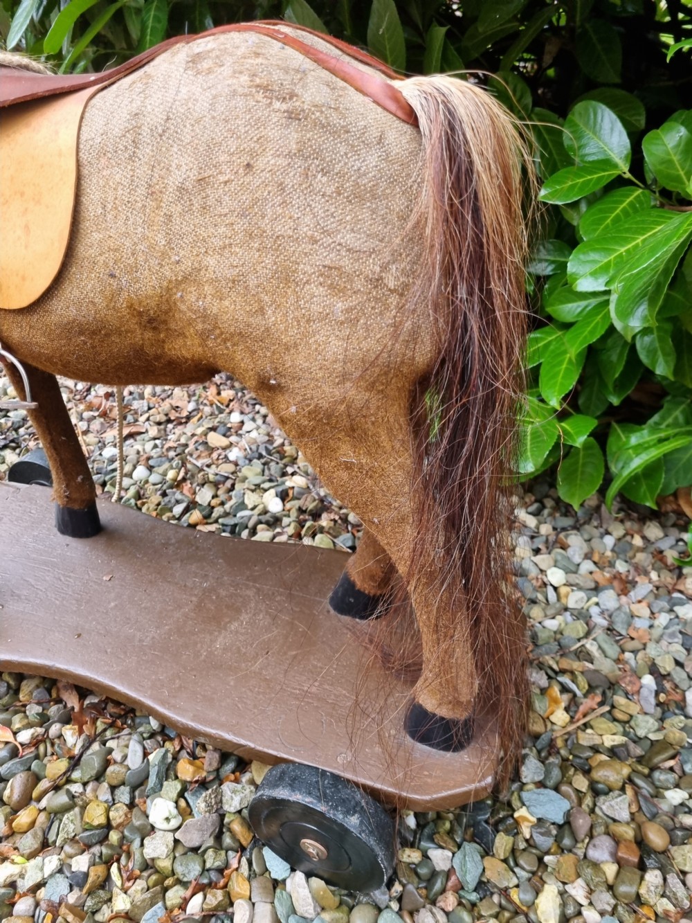 A late 19th-century childs pull-along toy horse with a tan fabric body, blonde mane, leather saddle, and bridle mounted on a brown wooden plinth with four wheels. View VII
