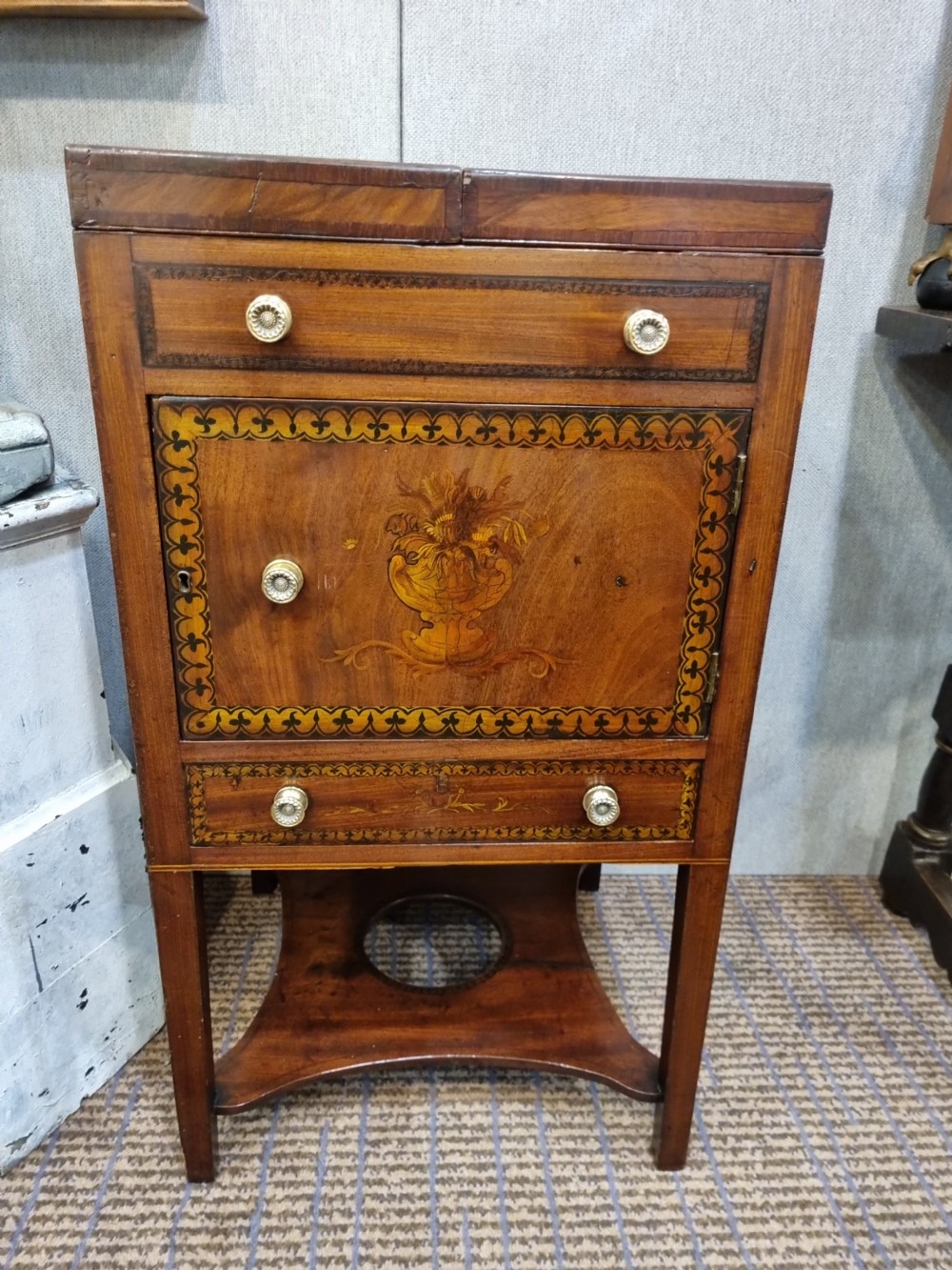 A Georgian mahogany night commode featuring intricate marquetry urn inlay on the main cupboard door, decorative floral border inlays, ceramic knobs, and a shaped base stretcher with a circular opening. View II