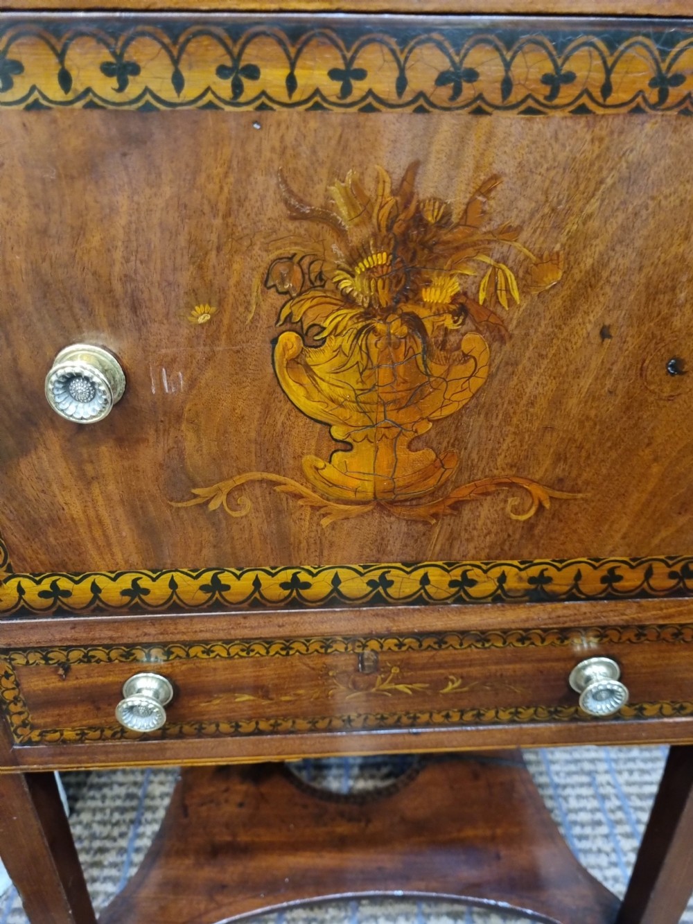 A Georgian mahogany night commode featuring intricate marquetry urn inlay on the main cupboard door, decorative floral border inlays, ceramic knobs, and a shaped base stretcher with a circular opening. View VI