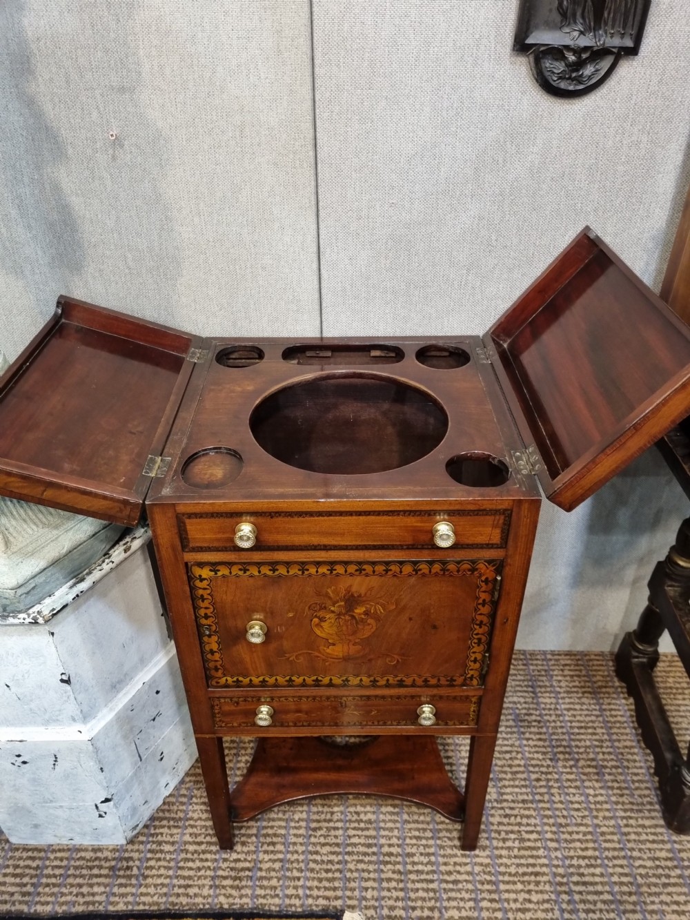 A Georgian mahogany night commode featuring intricate marquetry urn inlay on the main cupboard door, decorative floral border inlays, ceramic knobs, and a shaped base stretcher with a circular opening. View VIII