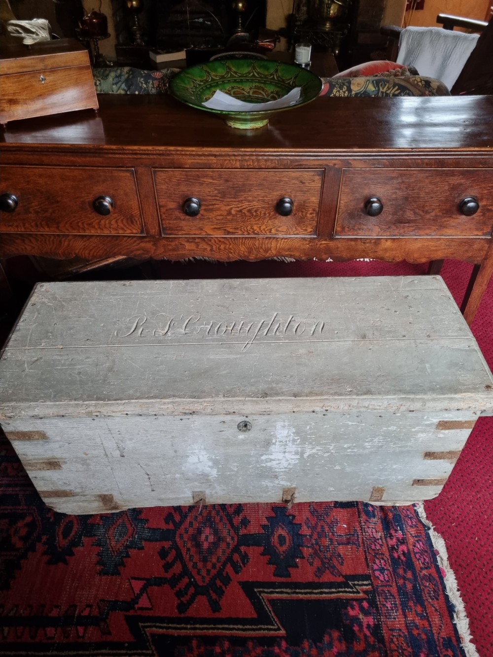 A 19th-century rectangular pine storage chest featuring weathered grey paint, iron corner bracing, metal side handles, and a flat hinged lid. View V