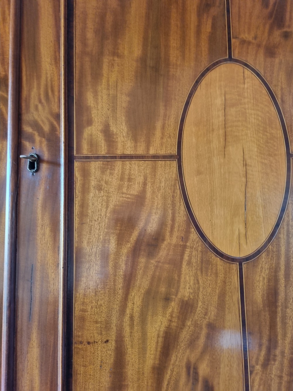 A late 18th-century mahogany secretaire cabinet featuring satinwood oval inlays on the doors, a pull-out writing drawer, and lower drawers with brass swan-neck handles. View IV