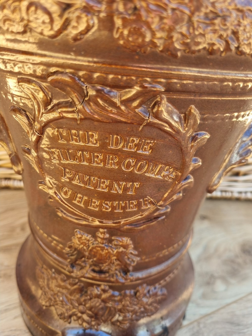 A dark brown glazed stoneware water filter featuring decorative relief moulding, a domed lid, maker markings reading Dee Filter Company Chester, and a spigot opening at the base. View II