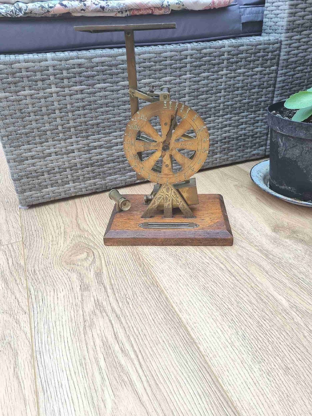 An antique brass post office parcel scale with a circular dial indicator mounted on a rectangular wooden base.