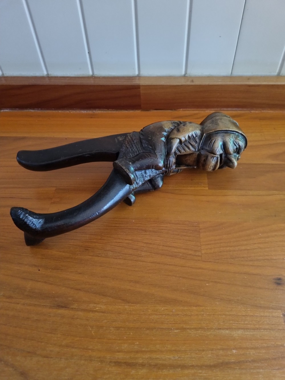 A hand-carved dark walnut nutcracker depicting a figurative hooded character with a lever mechanism. View V