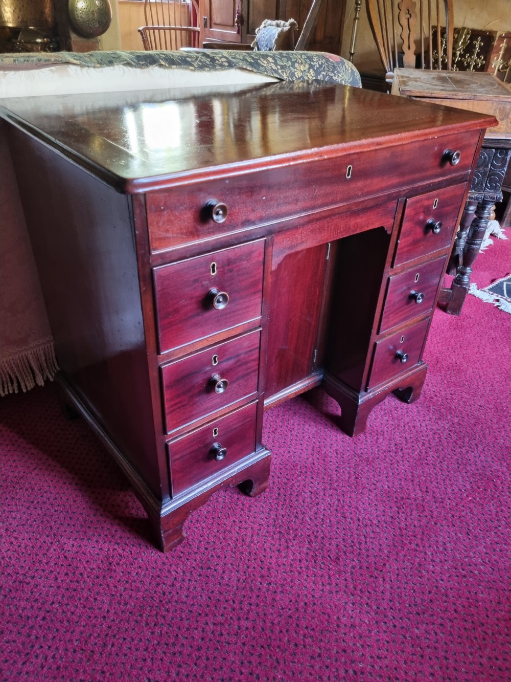 An 18th-century mahogany kneehole desk featuring a long top drawer above six smaller side drawers and a central recessed cupboard on bracket feet. View V