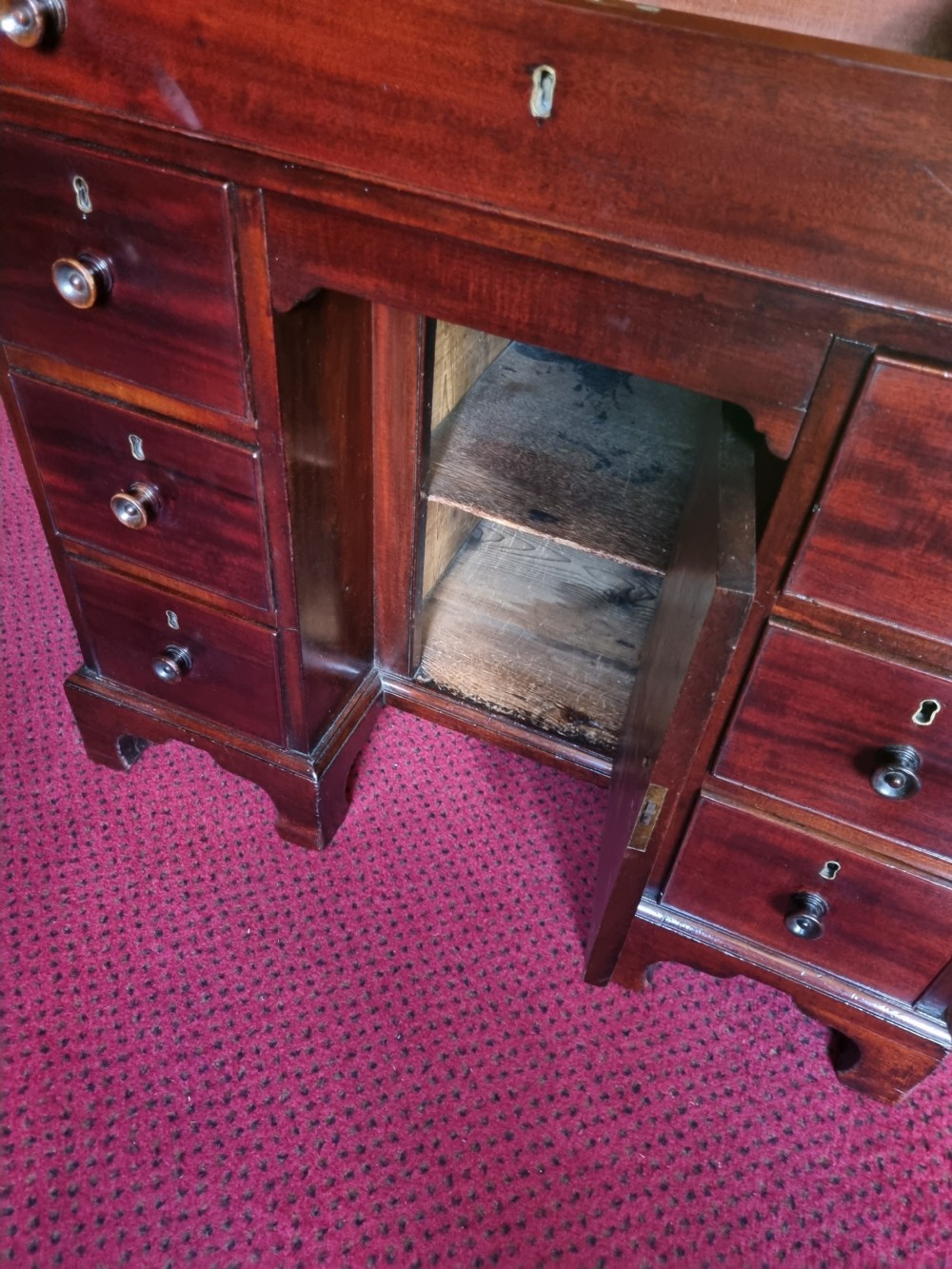 An 18th-century mahogany kneehole desk featuring a long top drawer above six smaller side drawers and a central recessed cupboard on bracket feet. View VIII