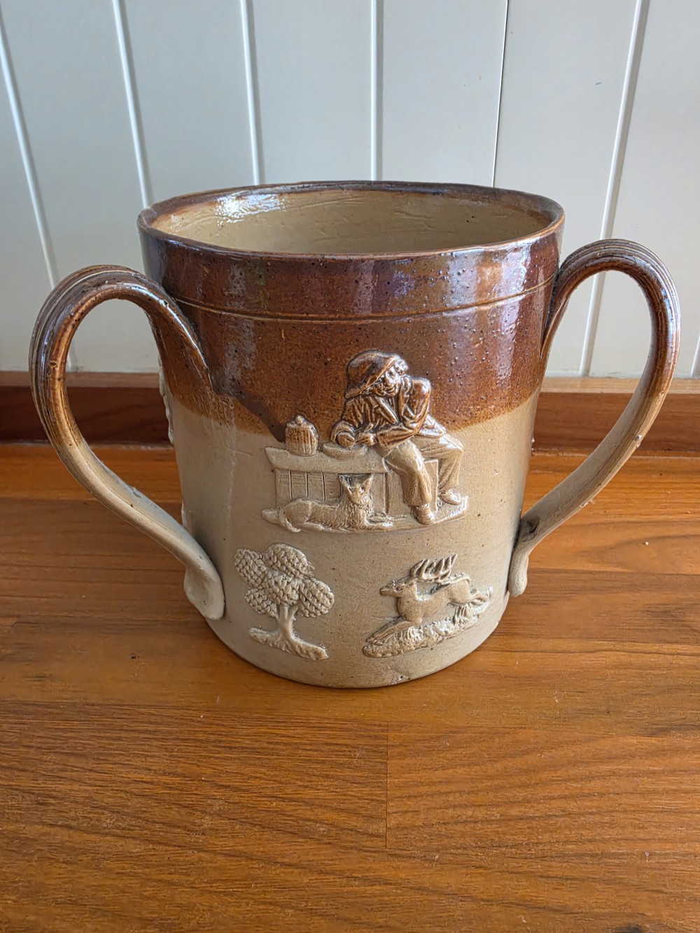 An early nineteenth-century two-tone salt-glazed stoneware tyg featuring three ribbed loop handles and raised relief sprigged decorations of tavern scenes and hunting hounds. View II