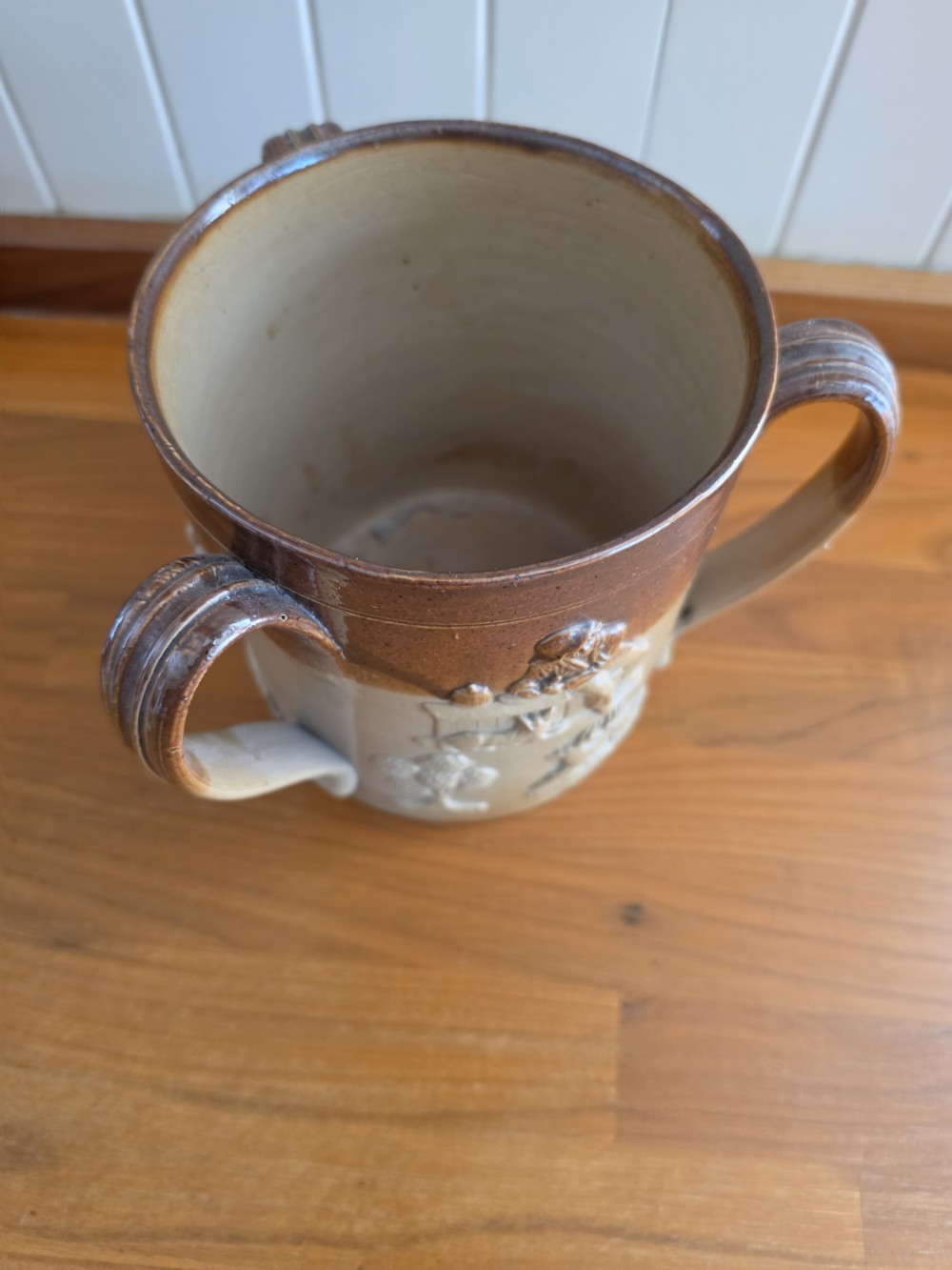An early nineteenth-century two-tone salt-glazed stoneware tyg featuring three ribbed loop handles and raised relief sprigged decorations of tavern scenes and hunting hounds. View III