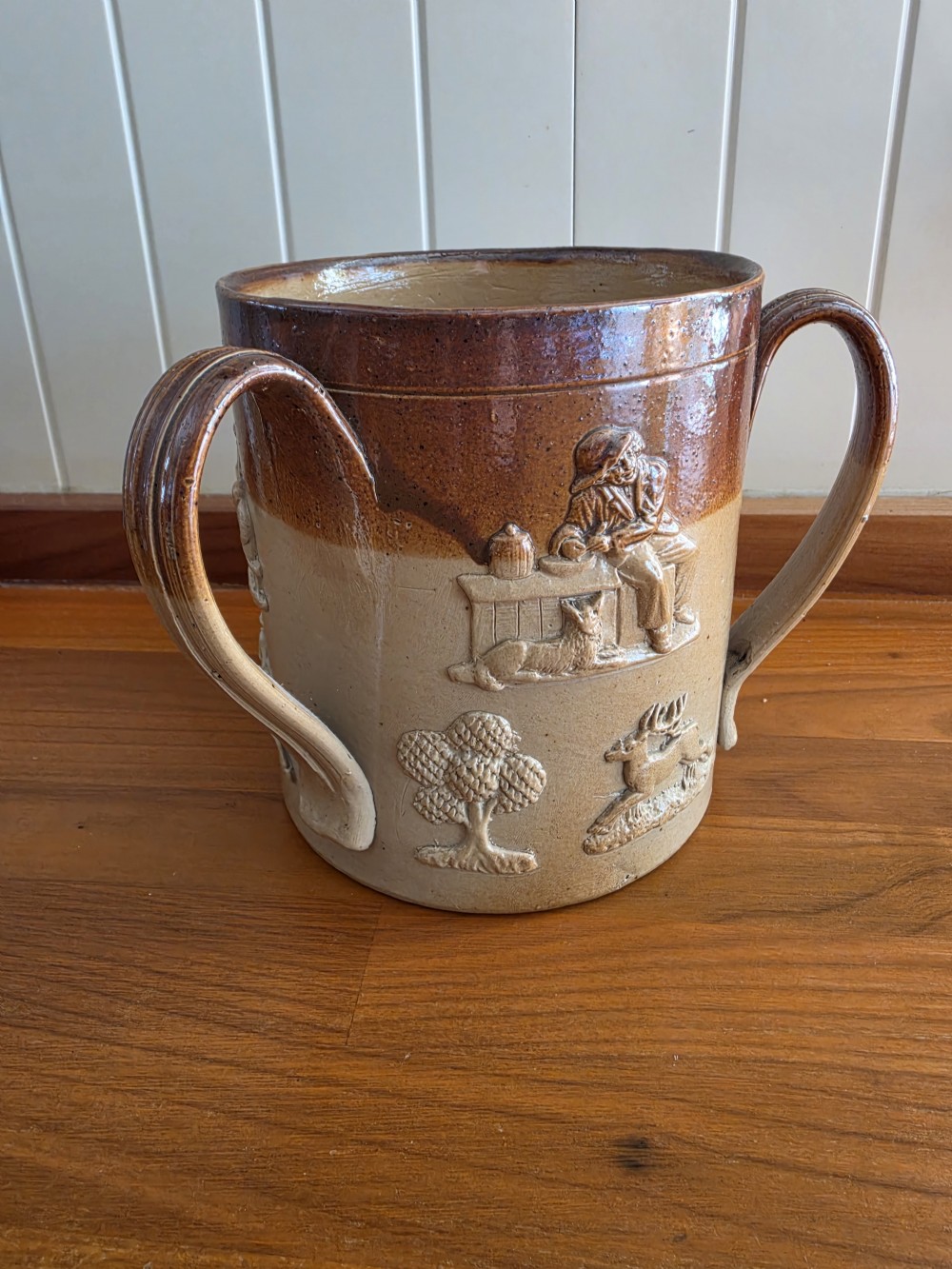 An early nineteenth-century two-tone salt-glazed stoneware tyg featuring three ribbed loop handles and raised relief sprigged decorations of tavern scenes and hunting hounds. View V
