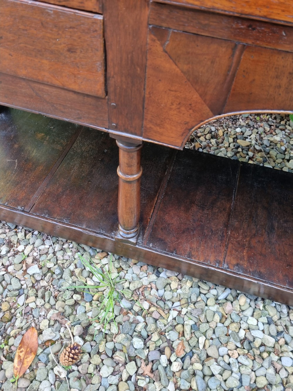 An eighteenth-century dark oak Welsh dresser base featuring five drawers with brass swan-neck handles, an arched central apron, turned supports, and a lower pot board shelf. View V