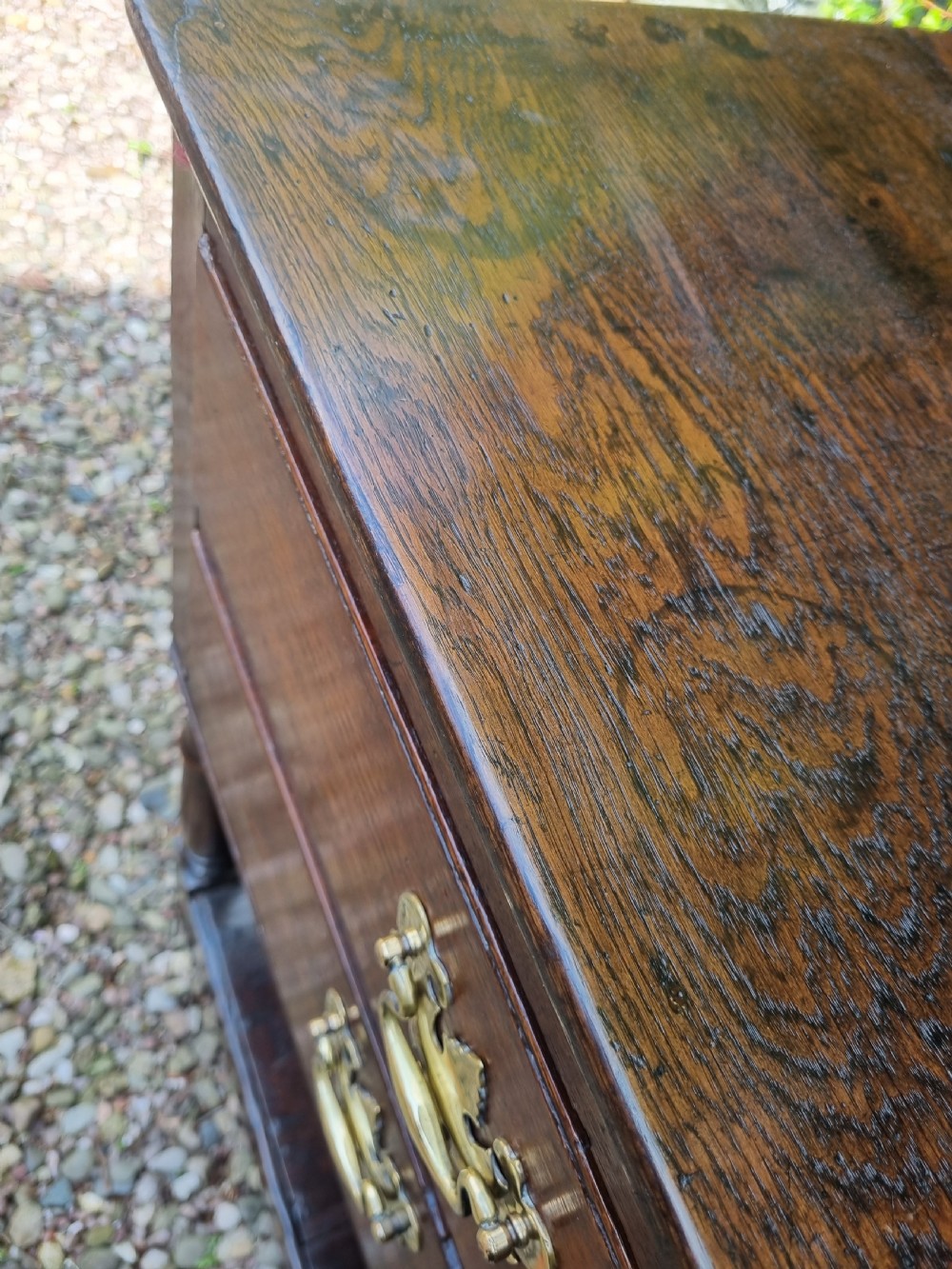 An eighteenth-century dark oak Welsh dresser base featuring five drawers with brass swan-neck handles, an arched central apron, turned supports, and a lower pot board shelf. View VI