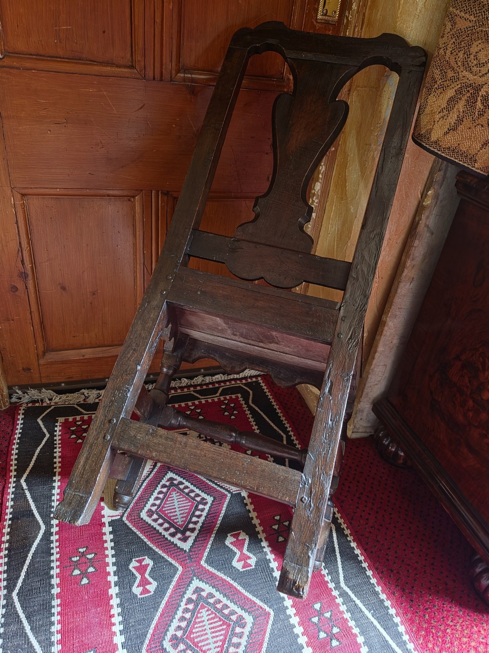 An 18th-century dark oak side chair featuring a vase-shaped splat back, solid timber seat, and turned front legs and stretcher. View V