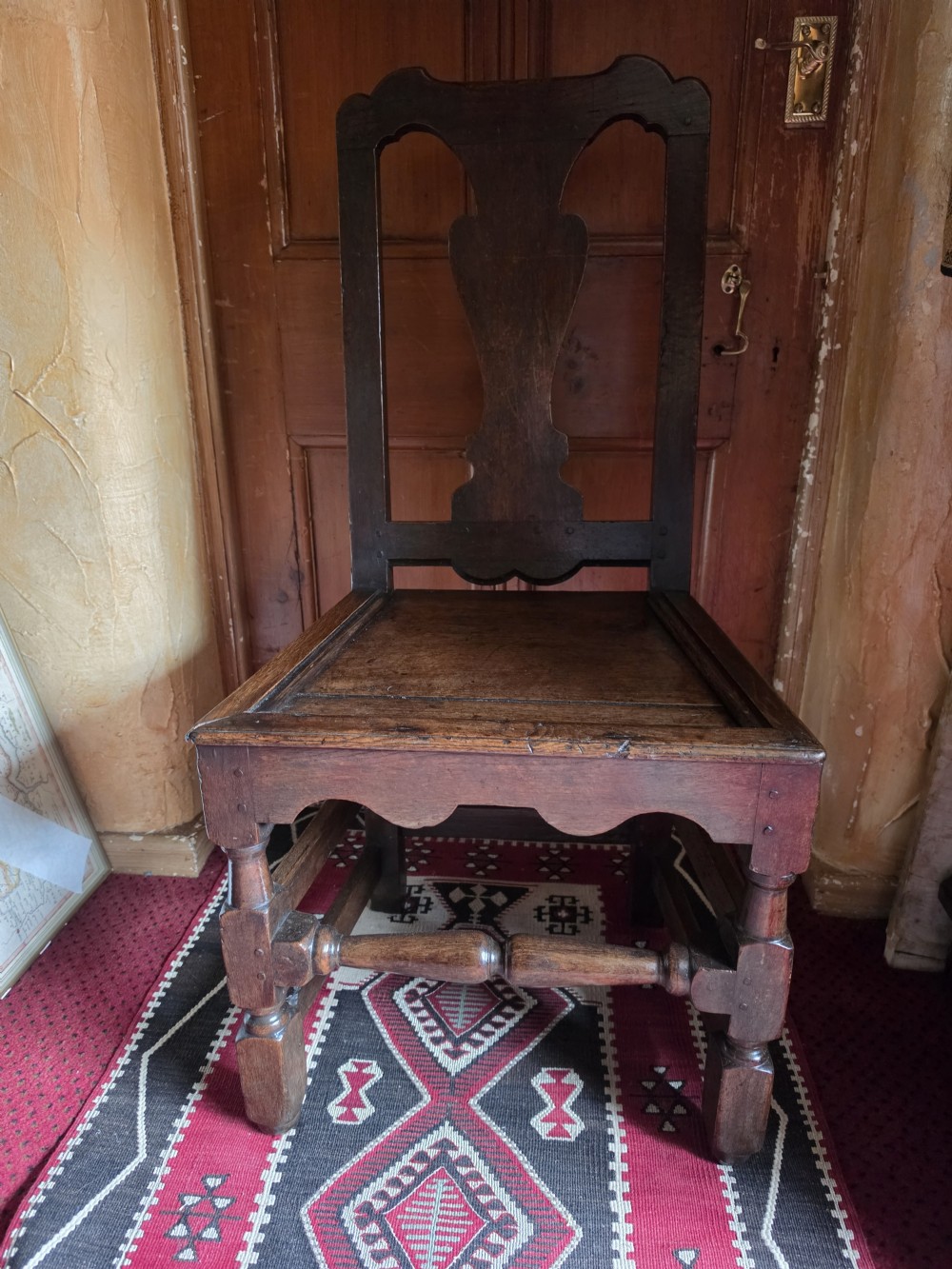 An 18th-century dark oak side chair featuring a vase-shaped splat back, solid timber seat, and turned front legs and stretcher. View VI