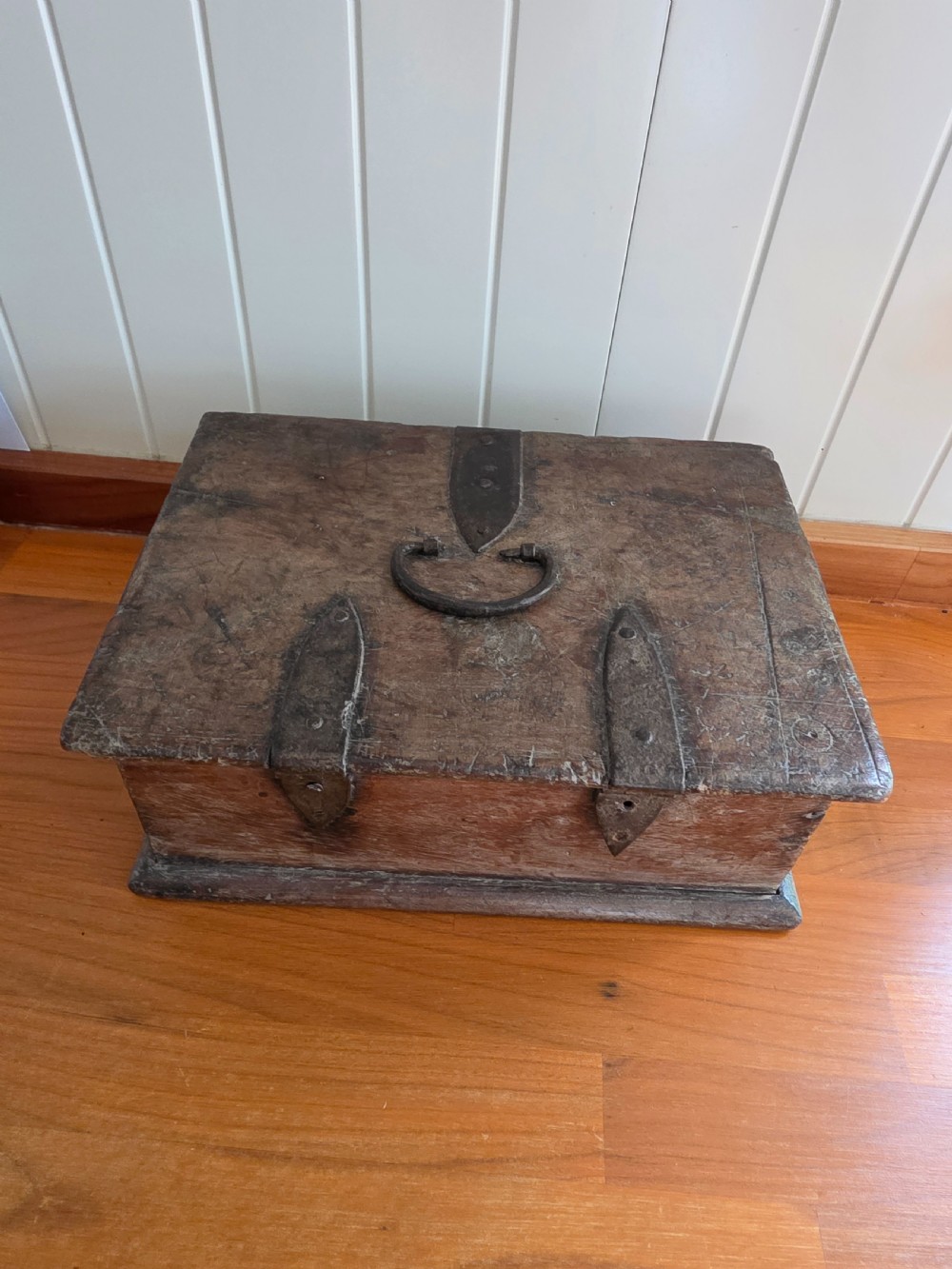 A small 17th-century style oak strong box with a hinged lid, top iron carrying handle, and heavy front wrought iron lock plate. View II