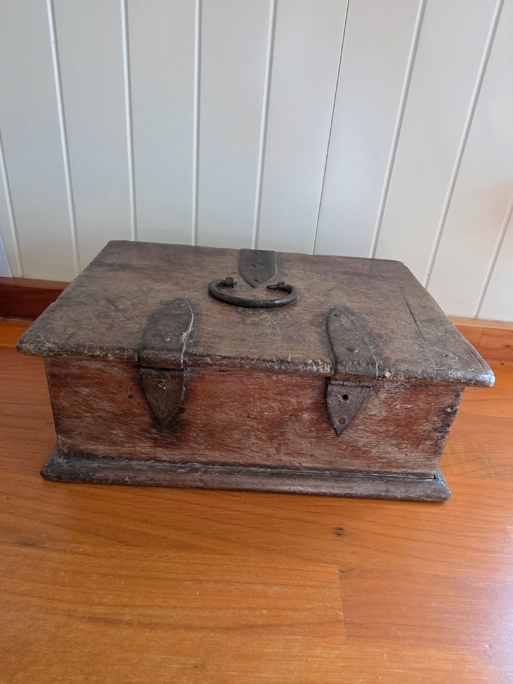 A small 17th-century style oak strong box with a hinged lid, top iron carrying handle, and heavy front wrought iron lock plate. View VI