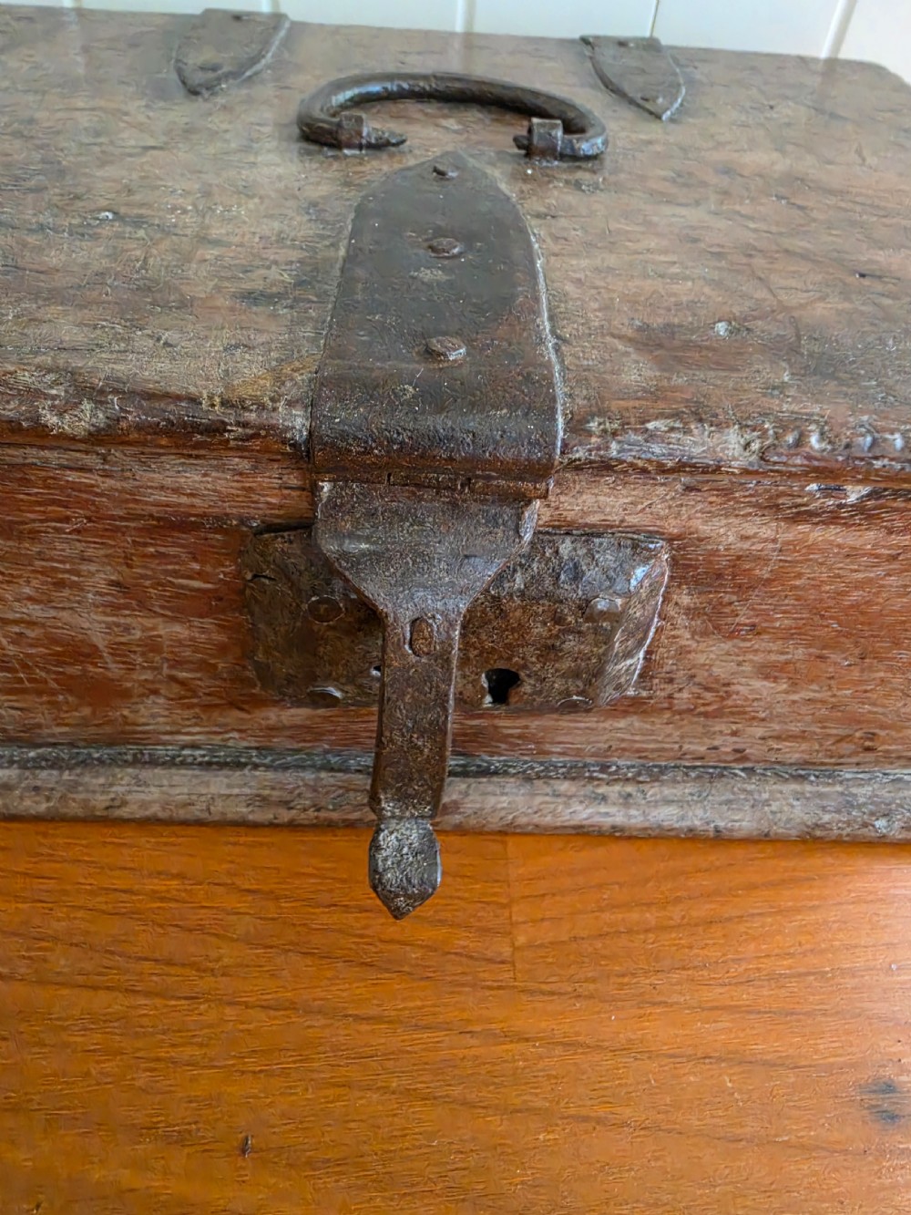 A small 17th-century style oak strong box with a hinged lid, top iron carrying handle, and heavy front wrought iron lock plate. View VII