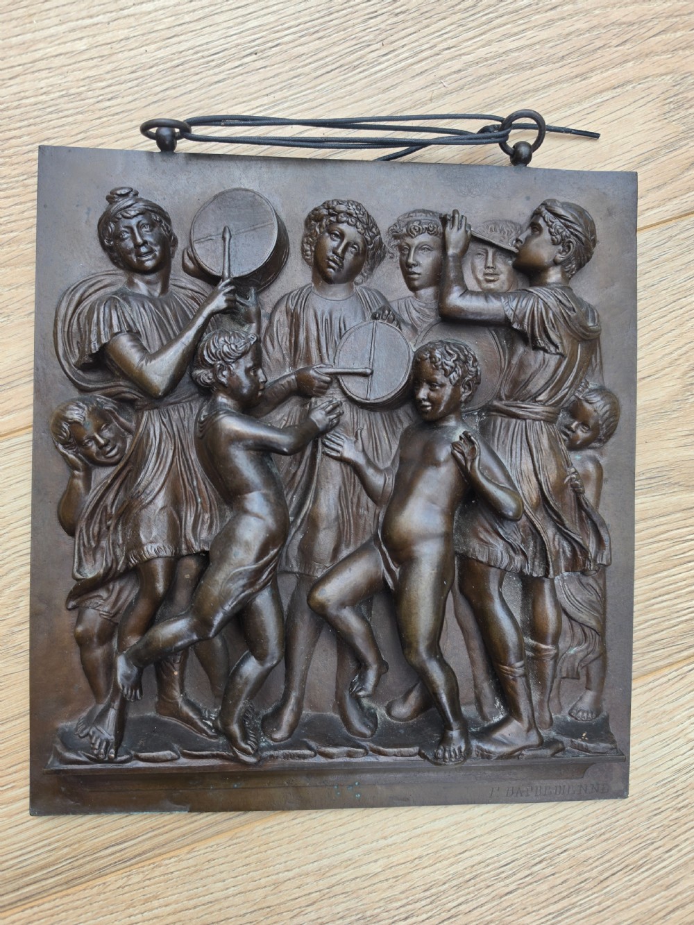 A square dark brown bronze relief plaque featuring cast figures playing musical instruments and dancing, signed F. Barbedienne at the lower right.