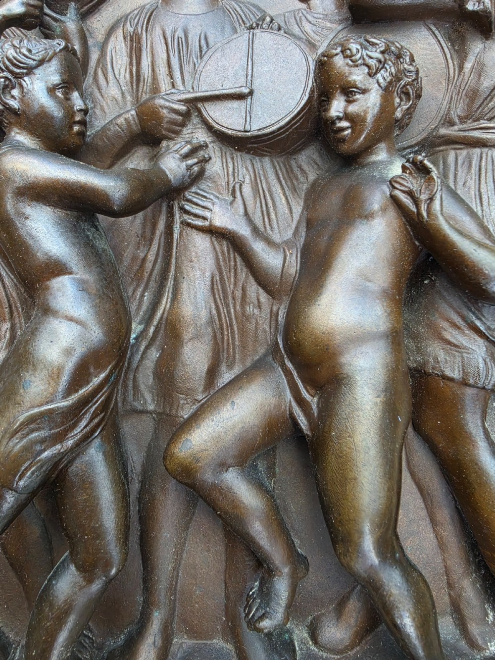 A square dark brown bronze relief plaque featuring cast figures playing musical instruments and dancing, signed F. Barbedienne at the lower right. View V