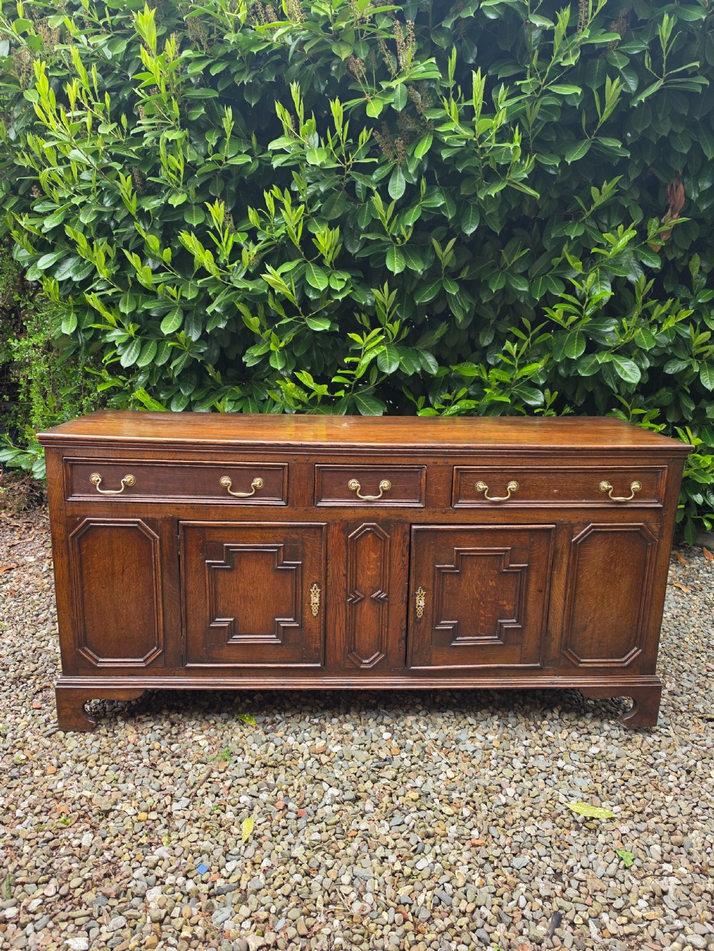 A Georgian dark oak dresser base featuring three top drawers over geometric moulded panel doors on bracket feet.