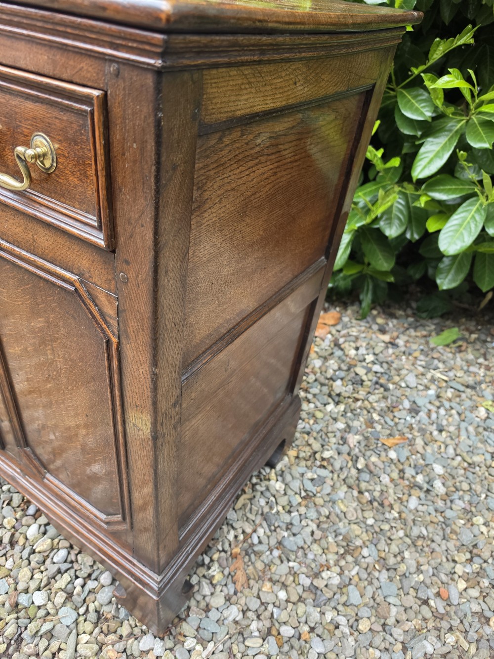 A Georgian dark oak dresser base featuring three top drawers over geometric moulded panel doors on bracket feet. View II