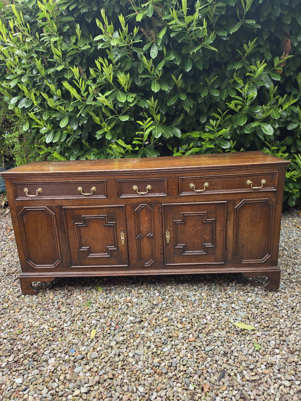 A Georgian dark oak dresser base featuring three top drawers over geometric moulded panel doors on bracket feet. View V