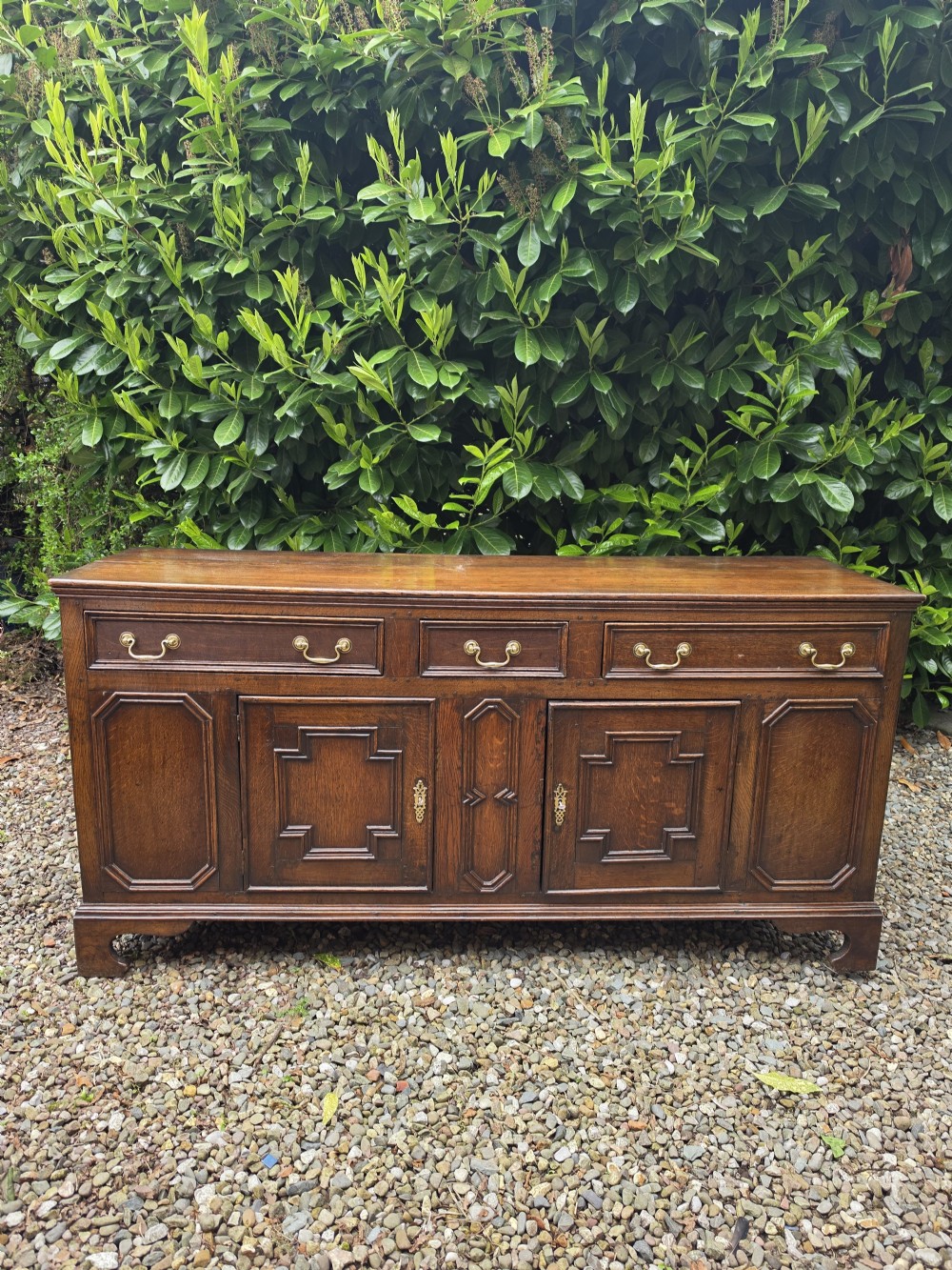 A Georgian dark oak dresser base featuring three top drawers over geometric moulded panel doors on bracket feet. View IX