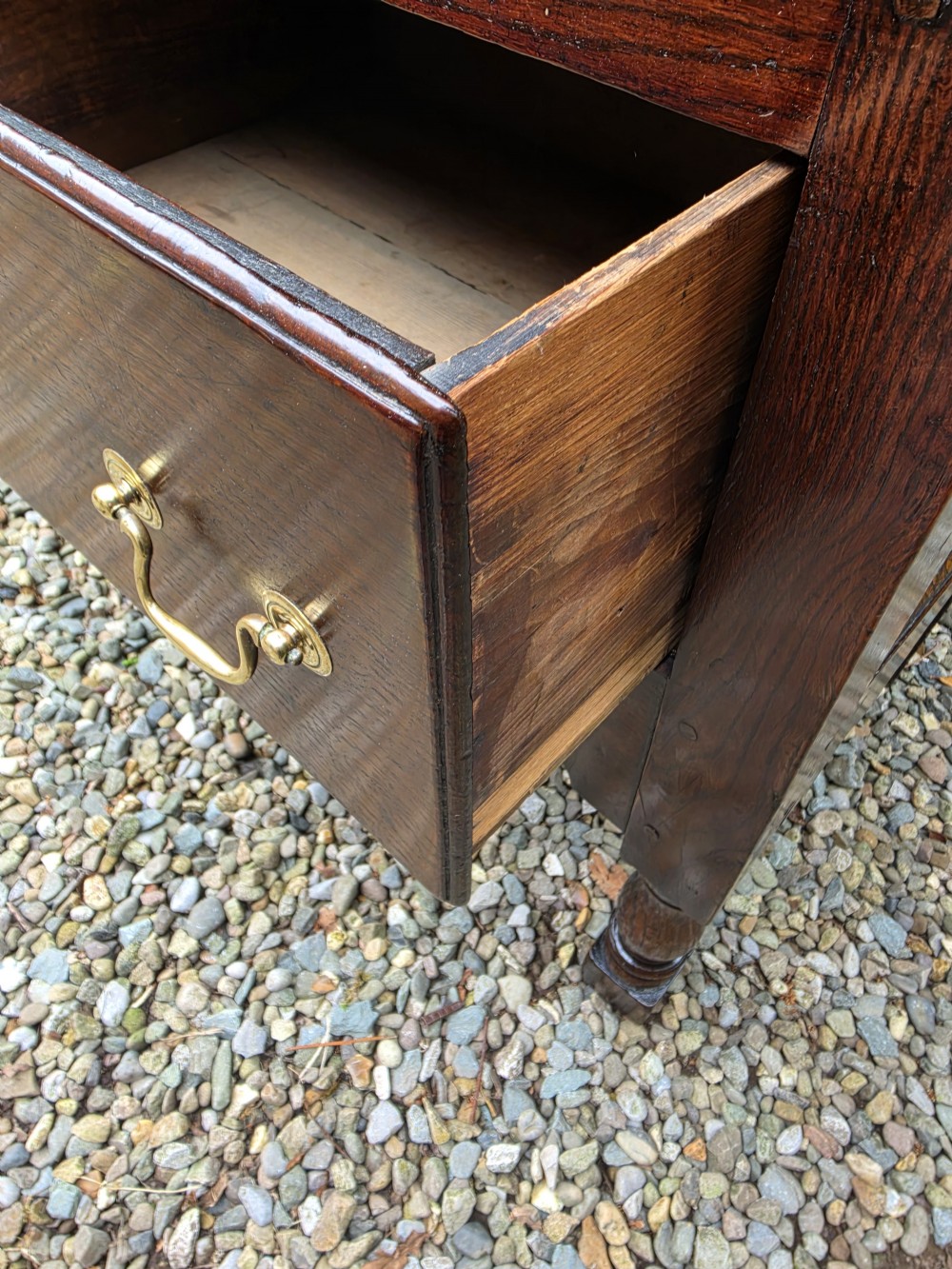 A mid-18th-century Georgian oak dresser base featuring three frieze drawers with brass swan-neck handles, a shaped apron, and turned front legs. View III