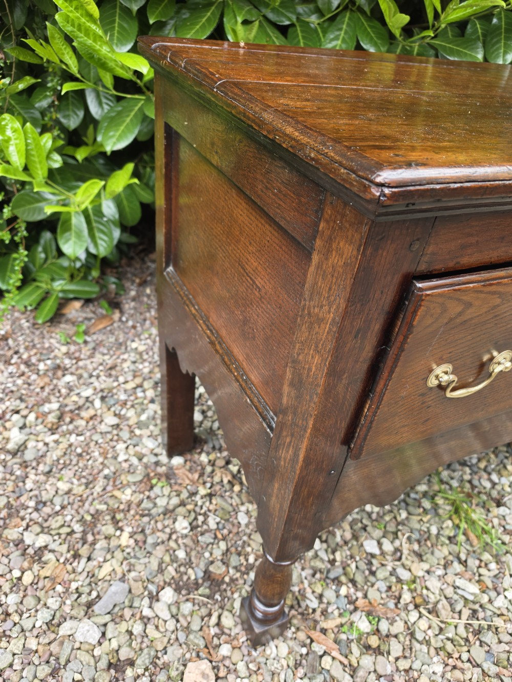 A mid-18th-century Georgian oak dresser base featuring three frieze drawers with brass swan-neck handles, a shaped apron, and turned front legs. View V
