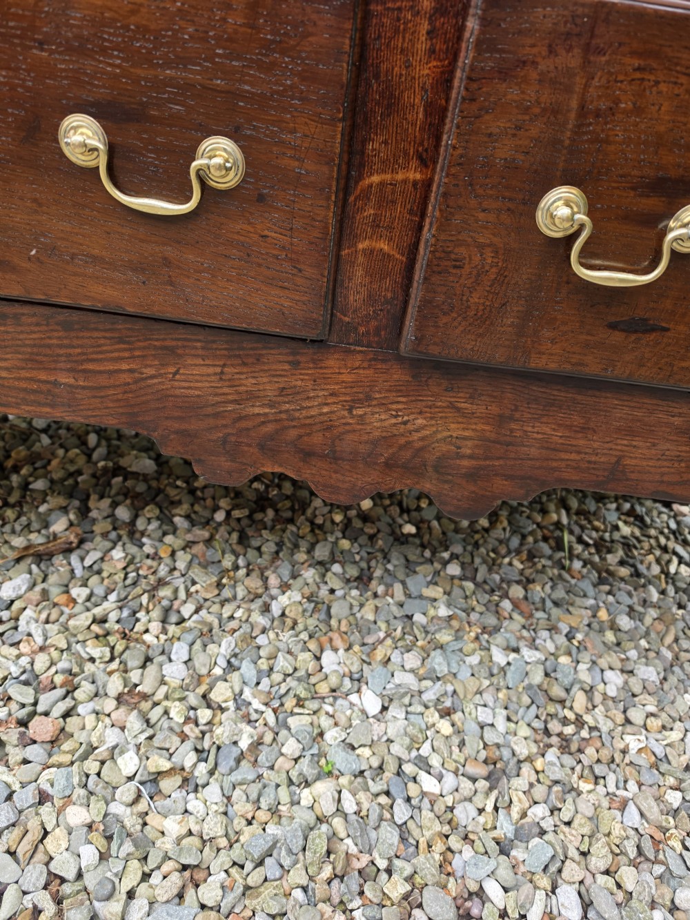 A mid-18th-century Georgian oak dresser base featuring three frieze drawers with brass swan-neck handles, a shaped apron, and turned front legs. View VI