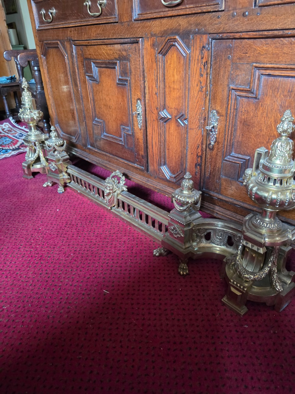 An ornate Louis XVI style brass fireplace fender featuring urn finials, classical mask details, and a pierced decorative rail. View IV