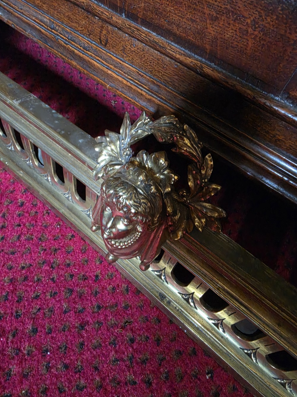 An ornate Louis XVI style brass fireplace fender featuring urn finials, classical mask details, and a pierced decorative rail. View III
