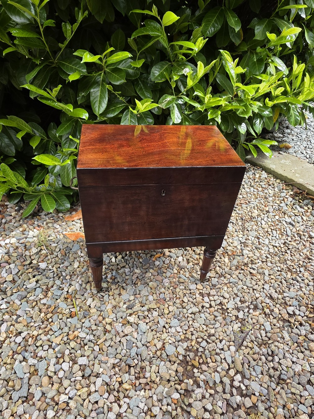 A dark Georgian mahogany cellaret chest featuring a flat hinged lid, central brass keyhole escutcheon, side carrying handles, and four turned legs. View III