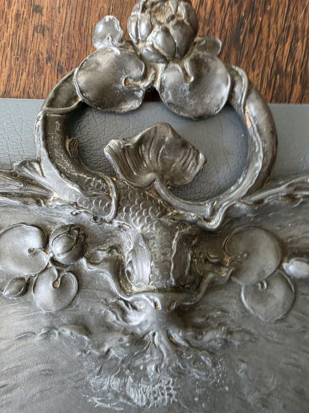 An antique Art Nouveau pewter crumb tray by Orivit featuring relief carvings of water lilies and a stylised aquatic design on a grey metal surface. View II
