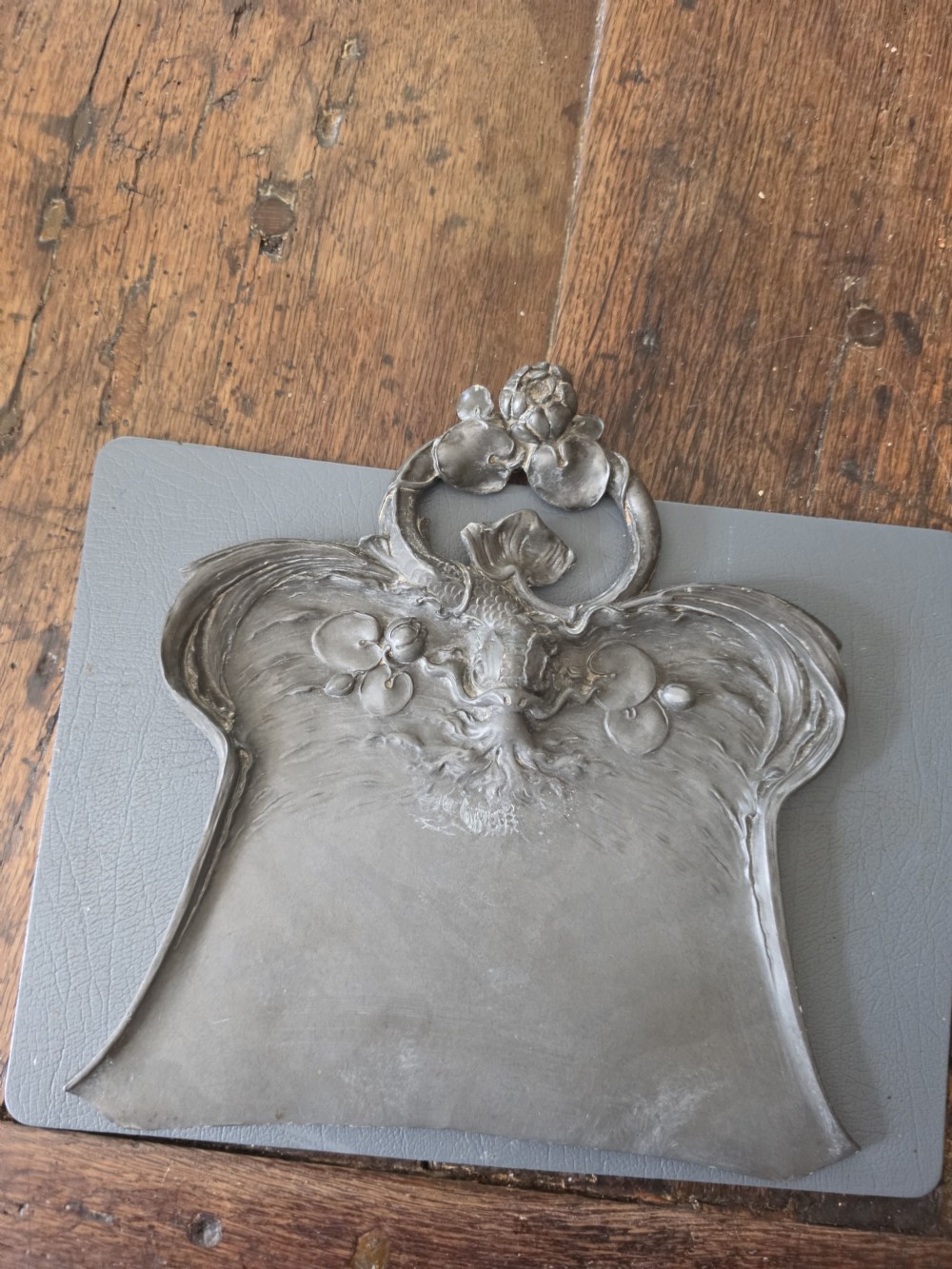 An antique Art Nouveau pewter crumb tray by Orivit featuring relief carvings of water lilies and a stylised aquatic design on a grey metal surface. View IV