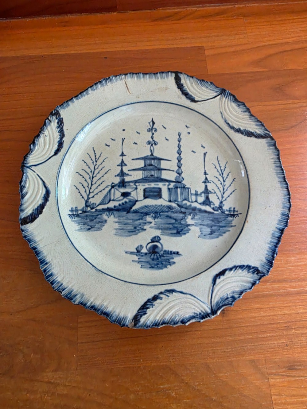 A late 18th-century circular pearlware plate decorated with hand-painted blue chinoiserie landscape motifs and a scalloped moulded rim.