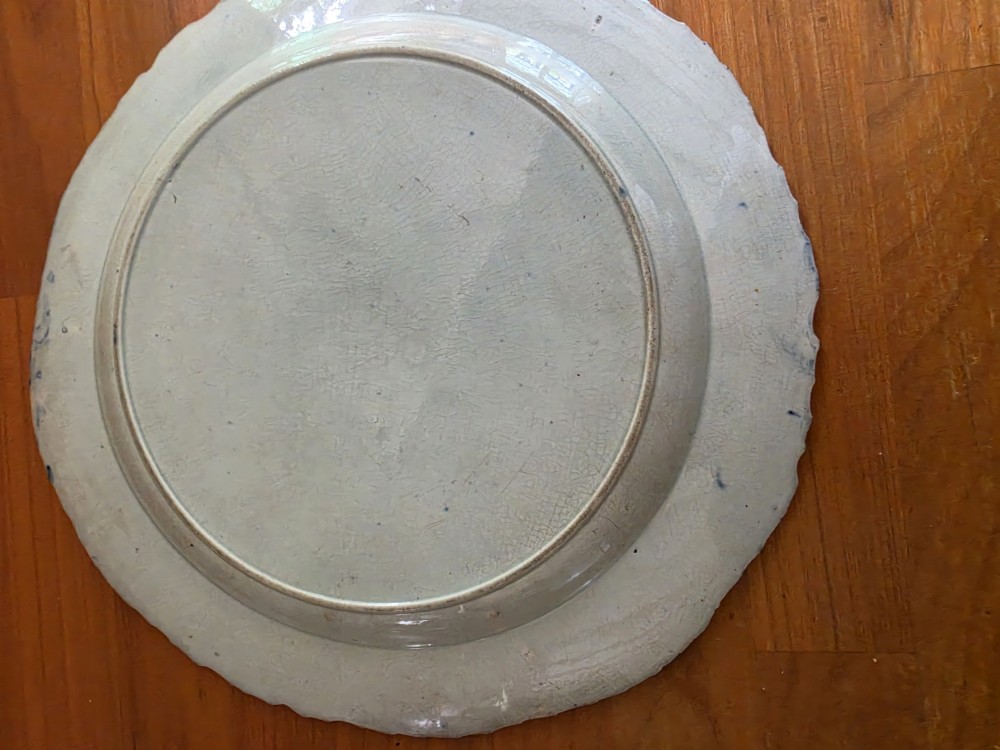 A late 18th-century circular pearlware plate decorated with hand-painted blue chinoiserie landscape motifs and a scalloped moulded rim. View II