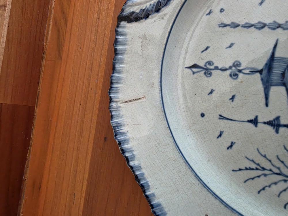 A late 18th-century circular pearlware plate decorated with hand-painted blue chinoiserie landscape motifs and a scalloped moulded rim. View III