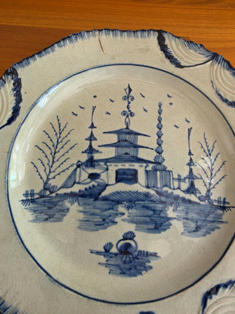 A late 18th-century circular pearlware plate decorated with hand-painted blue chinoiserie landscape motifs and a scalloped moulded rim. View IV