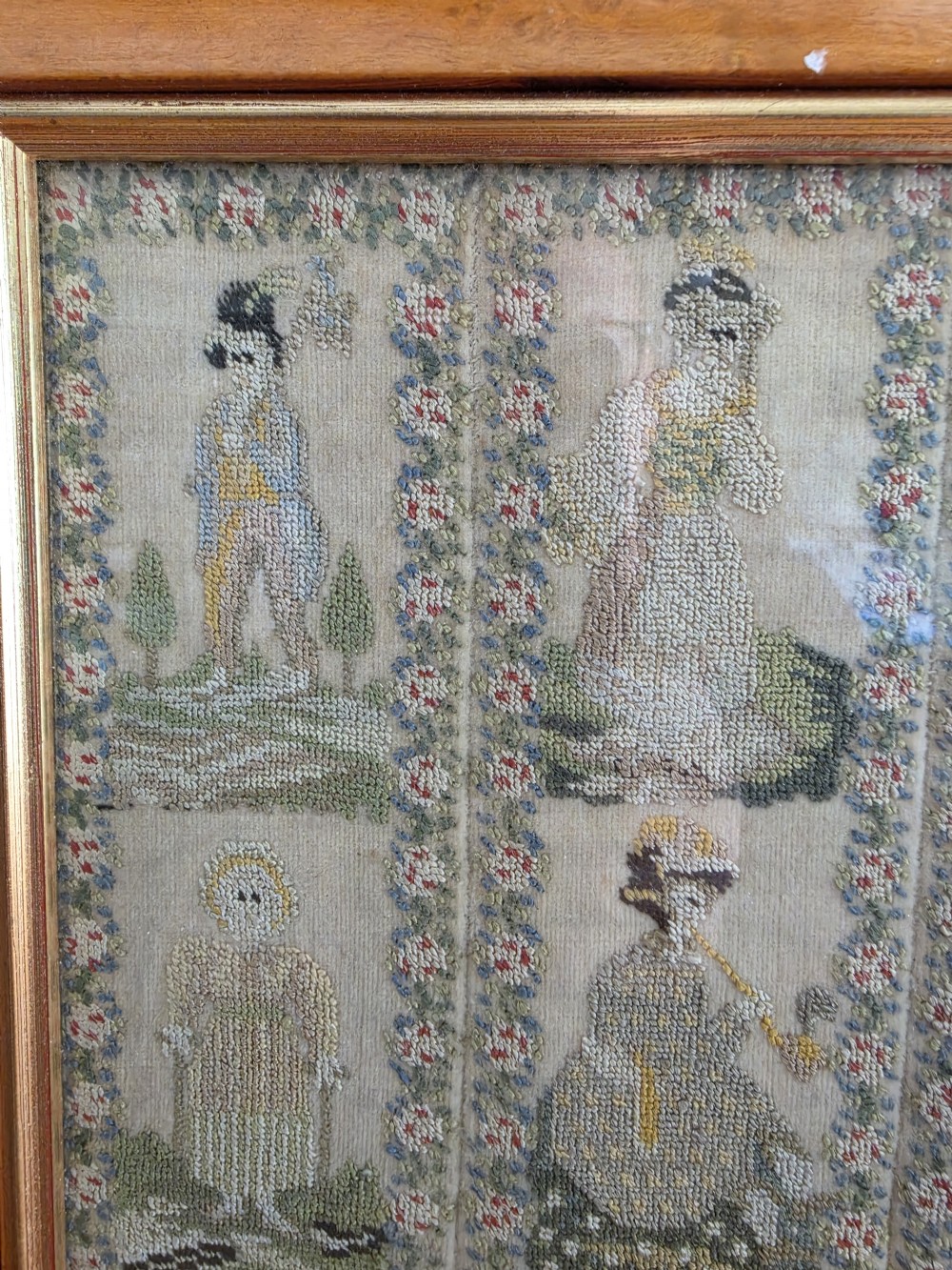 A framed Georgian silk needlework sampler featuring sixteen individual figures in historical costume, framed within floral column borders and a timber frame. View V