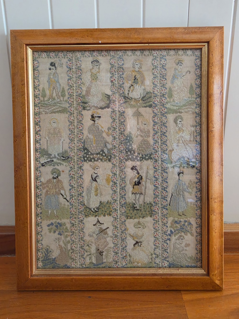 A framed Georgian silk needlework sampler featuring sixteen individual figures in historical costume, framed within floral column borders and a timber frame. View VI