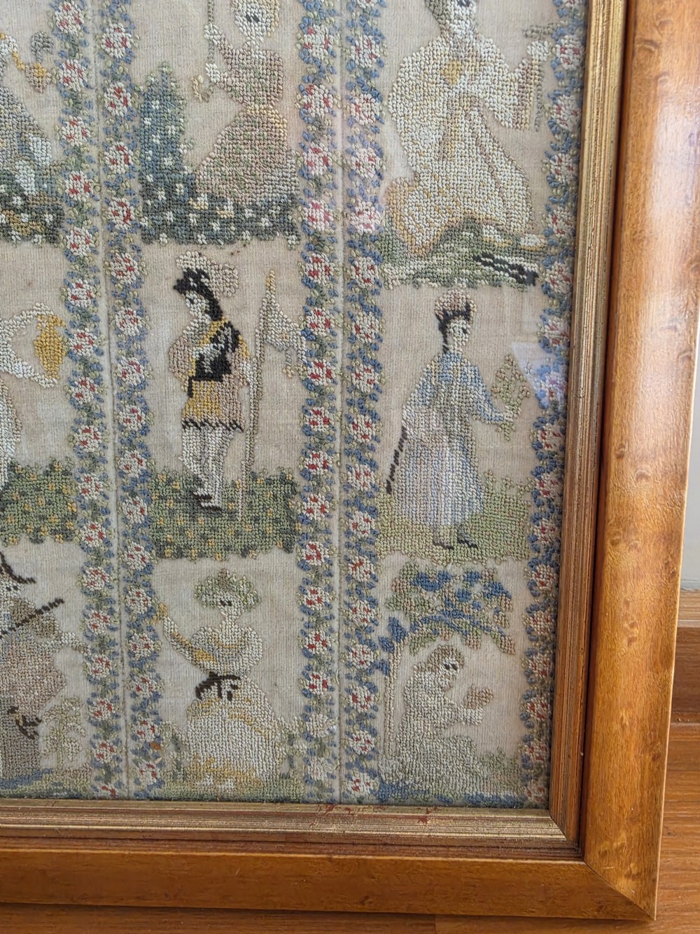 A framed Georgian silk needlework sampler featuring sixteen individual figures in historical costume, framed within floral column borders and a timber frame. View VIII