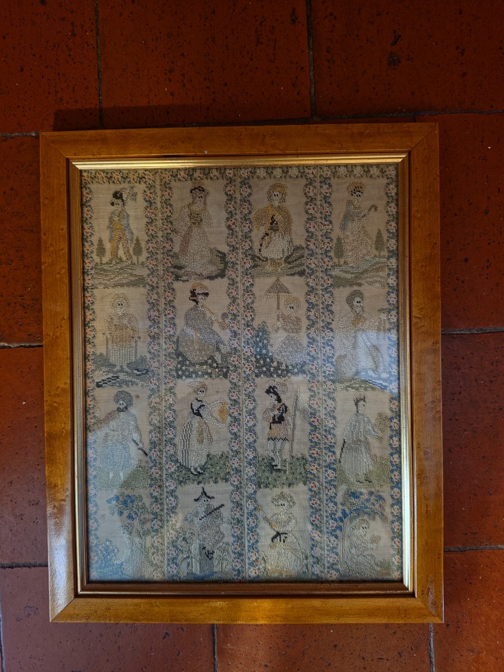 A framed Georgian silk needlework sampler featuring sixteen individual figures in historical costume, framed within floral column borders and a timber frame. View IX